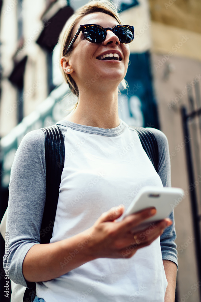 Aufkleber smiling hipster girl in sunglasses strolling in downtown using mobile phone application for navigate