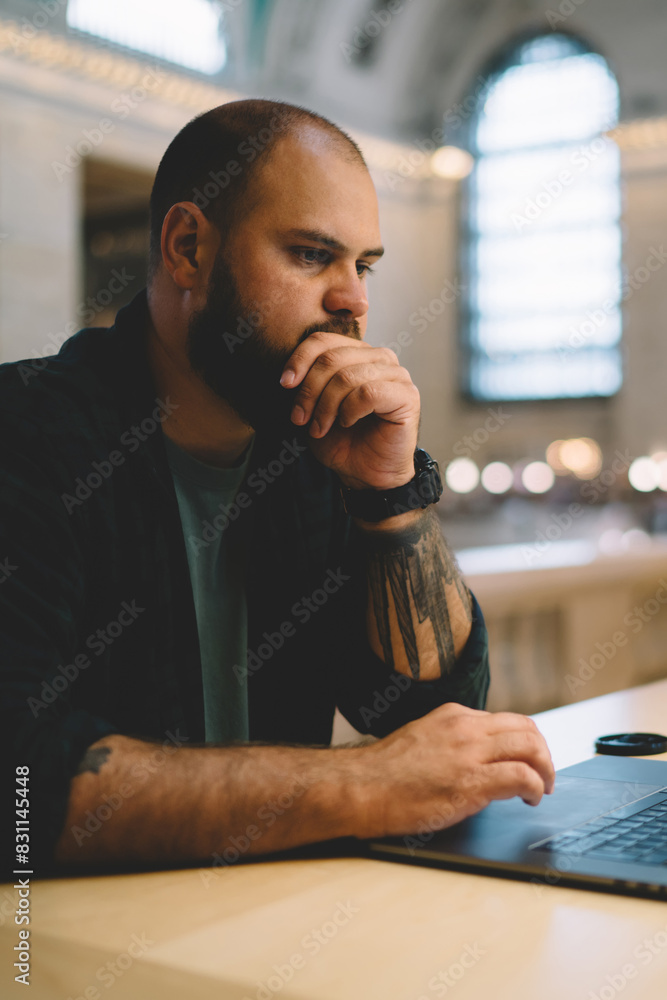 Poster pensive male student sitting in university library with laptop computer preparing for examinations,t
