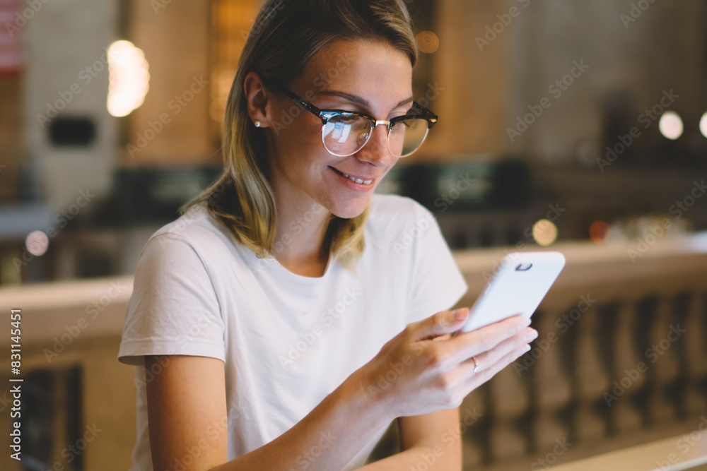 Aufkleber young hipster girl checking mail on smartphone spending time in library preparing report using lapto