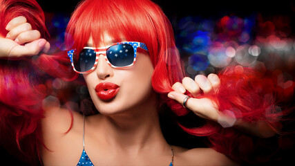 Red-haired woman celebrates 4th of July wearing American flag sunglasses and pouting her sensual...
