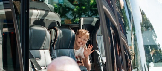 Smiling child waving hand from school bus window before trip. © Alena Vilgelm