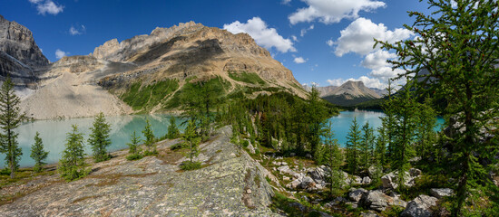 View along a rock ridge at a large rocky mountain and two blue lakes. The blue sky has scattered...