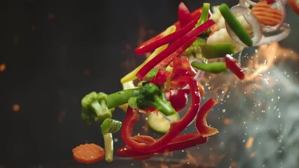 Closeup of chef preparing and throwing vegetable mix on frying pan on fire. Preparation fresh appetizing food. Vegetables flying into the pan in slow motion. Healthy vegetarian food cooking close-up