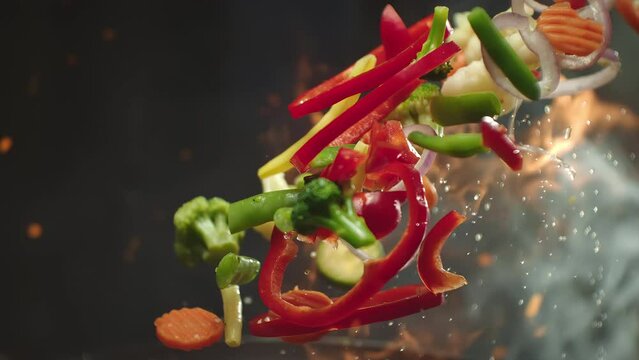 Closeup of chef preparing and throwing vegetable mix on frying pan on fire. Preparation fresh appetizing food. Vegetables flying into the pan in slow motion. Healthy vegetarian food cooking close-up