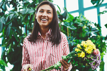 Happy asian female botanist satisfied with work in greenhouse making beautiful bouquets from fresh...