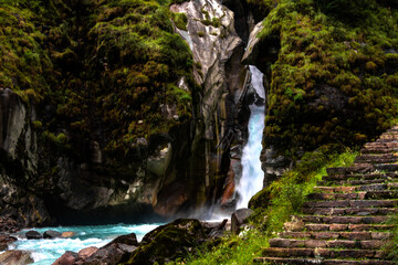 Fototapeta premium Waterfall among the himalaya mountains with green forest and a river full of rocks.