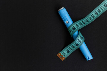 Ozempic injector drug pen with a measuring tape on a black background. Anti diabetes and lower blood sugar levels. Weight loss concept
