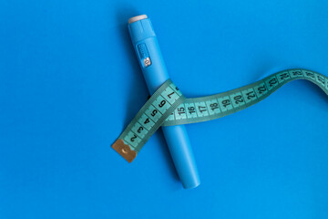 Ozempic injector drug with a measuring tape on a blue background. Anti diabetes and lower blood sugar levels. Weight loss concept