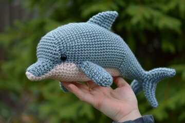 Obraz premium Closeup of a hand holding a cute crocheted dolphin toy with a blurred background