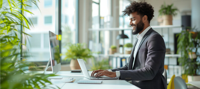 a  of a multiracial mid-adult businessman with a beard standing and smiling at his desk, reviewing data on a laptop in a bright business office, wearing a suit, multi