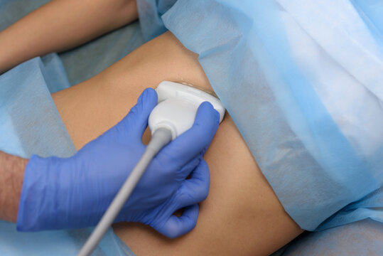 A doctor using an ultrasound transducer performs an ultrasound examination. Ultrasound scanner on a woman&rsquo;s stomach, ultrasound of internal organs and abdominal cavity. Elastography and sonography.