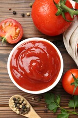 Delicious ketchup in bowl, tomatoes and peppercorns on wooden table, flat lay
