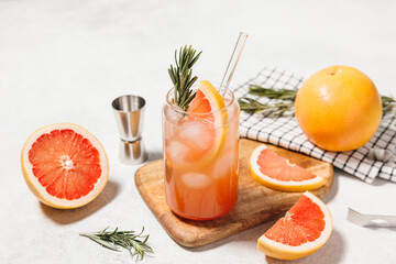 Grapefruit cocktail with rosemary garnish in a glass, served on a wooden cutting board. Vibrant, refreshing drink perfect for summer menu or cocktail recipes. Greyhound, lemonade, paloma, mocktail.