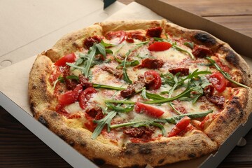 Tasty pizza with cheese, tomato and arugula in cardboard box on table