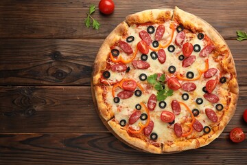 Tasty pizza with dry smoked sausages, tomatoes, olives, pepper and parsley on wooden table, top...