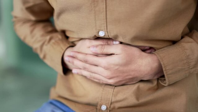 Close up. Male hands holding massaging stomach. Businessman in shirt feels stomach pain sitting at workplace in business office. Sick man worker suffers from bloating, gastritis, poisoning or bloating