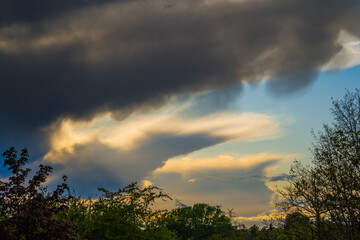 Ominous sunlit thunder clouds in blue sky over landscape