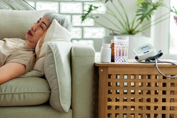 A woman is laying on a couch with a glass of water and a bottle of pills next to her