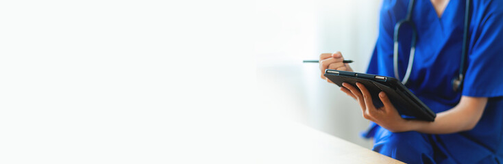 A nurse is sitting at a desk with a tablet in front of her. She is using a pen to write on the tablet