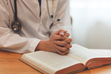 A doctor is praying while looking at a book. The book is open to a page with a cross on it
