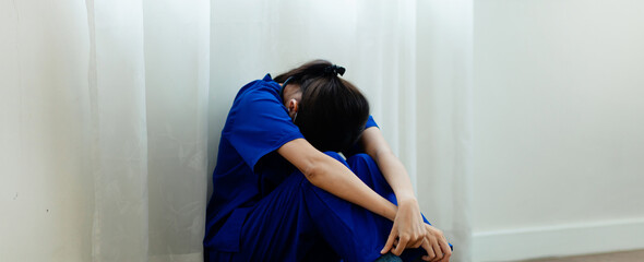 A woman in a blue scrubs is crying on the floor. She is wearing a blue shirt and blue pants