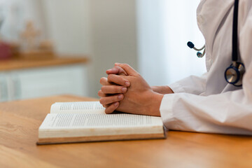 A doctor is praying while looking at a book. The book is open to a page with a cross on it