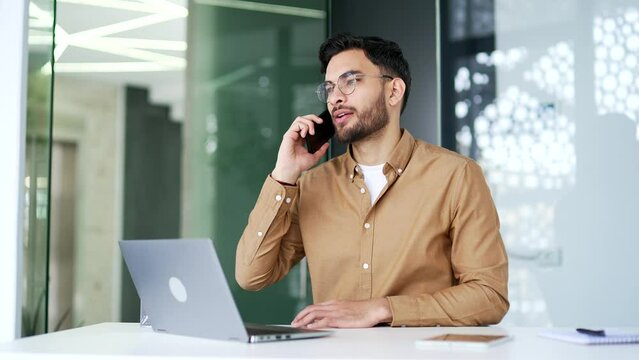 Handsome happy businessman talking on phone while sitting at a workplace in a office. Man worker seller communicates with a client, answers questions, conducts a conversation with a business partner