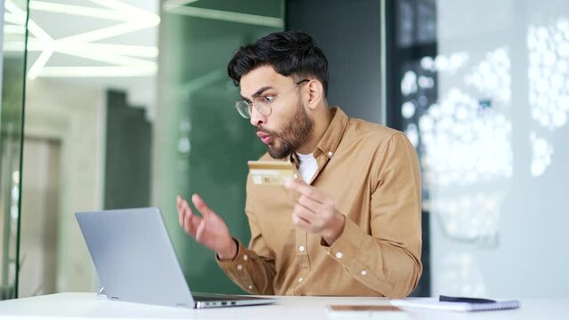 Shocked entrepreneur checks his credit card on laptop sitting at workplace in business office. Frustrated upset worker faced fraud, money was stolen from his account. Man became a victim of deception