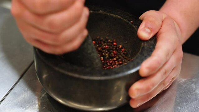 Close up of strong kitchener grinding assortment of peppercorns by hand in coarse mortar and pestle. Caucasian person crushing different types of grain for making author's spicy seasoning.