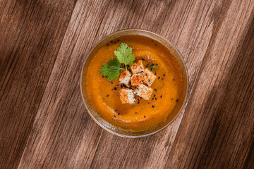 flat lay of one isolated bowl of pumpking orange soup with toppings over rustic wooden table