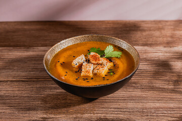 one isolated bowl of pumpking orange soup with toppings over rustic wooden table