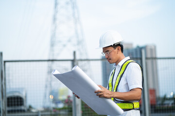 A man wearing a yellow vest and a hard hat is holding a blueprint. Concept of professionalism and...