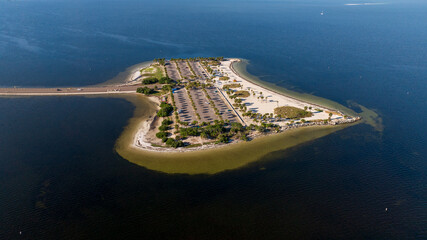 Aerial view of Fred Howard Park in Tarpon Springs, Florida, featuring parking lots, palm trees, sandy beaches, and surrounding blue waters under a clear sky.