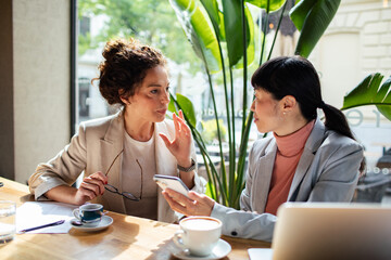 Two professional women discussing work at a cafe table