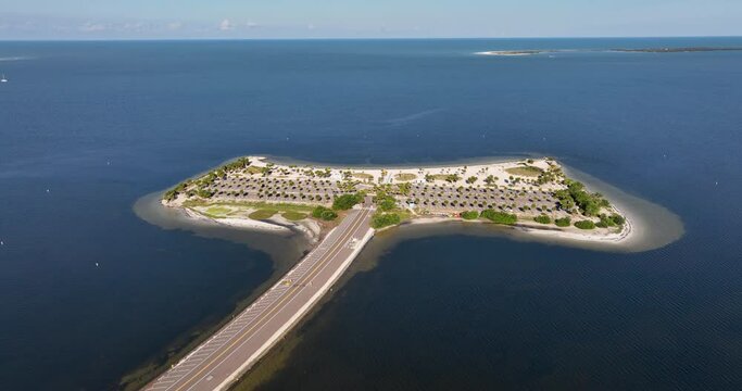 Aerial view of Fred Howard Park in Tarpon Springs, Florida, featuring parking lots, palm trees, sandy beaches, and surrounding blue waters under a clear sky.