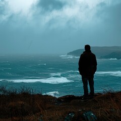 A silhouette of a man standing on a hill and looking at the waves of the autumn sea on a windy, overcast day, professional photo, saturated picture