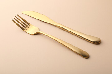 Stylish cutlery. Golden knife and fork on beige table