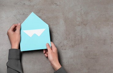 Woman holding letter envelope with card at grey textured table, top view. Space for text