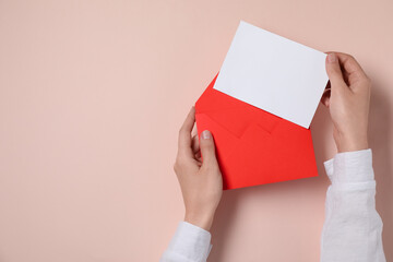 Woman taking card out of letter envelope at beige table, top view. Space for text