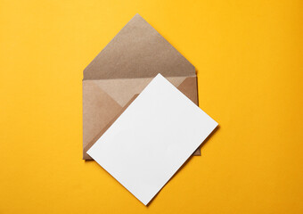 Blank sheet of paper and letter envelope on orange background, top view