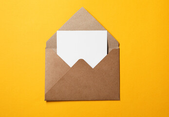 Blank sheet of paper in open letter envelope on orange background, top view