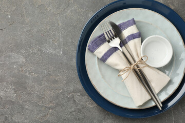 Stylish setting with cutlery, plates, bowl and napkin on grey textured table, top view. Space for text