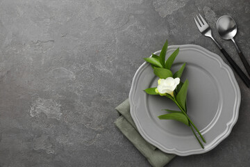 Stylish setting with cutlery, napkin, flower and plate on grey textured table, flat lay. Space for...