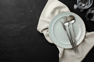 Stylish setting with cutlery, napkin and plate on dark textured table, flat lay. Space for text