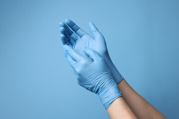 Doctor wearing medical gloves on light blue background, closeup