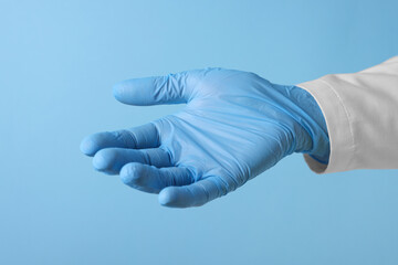 Doctor wearing medical glove holding something on light blue background, closeup