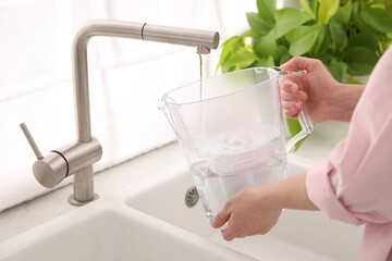 Woman filling filter jug with water from tap in kitchen, closeup
