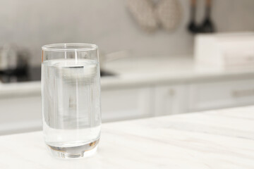 Glass with clear water on white marble table in kitchen, space for text