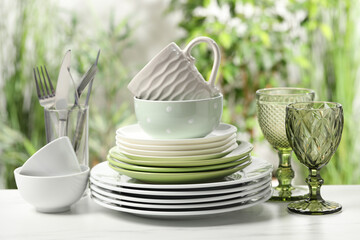 Beautiful ceramic dishware, glasses, cutlery and cup on white marble table outdoors