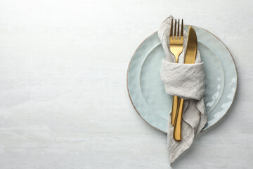 Stylish setting with cutlery, napkin and plates on white table, top view. Space for text